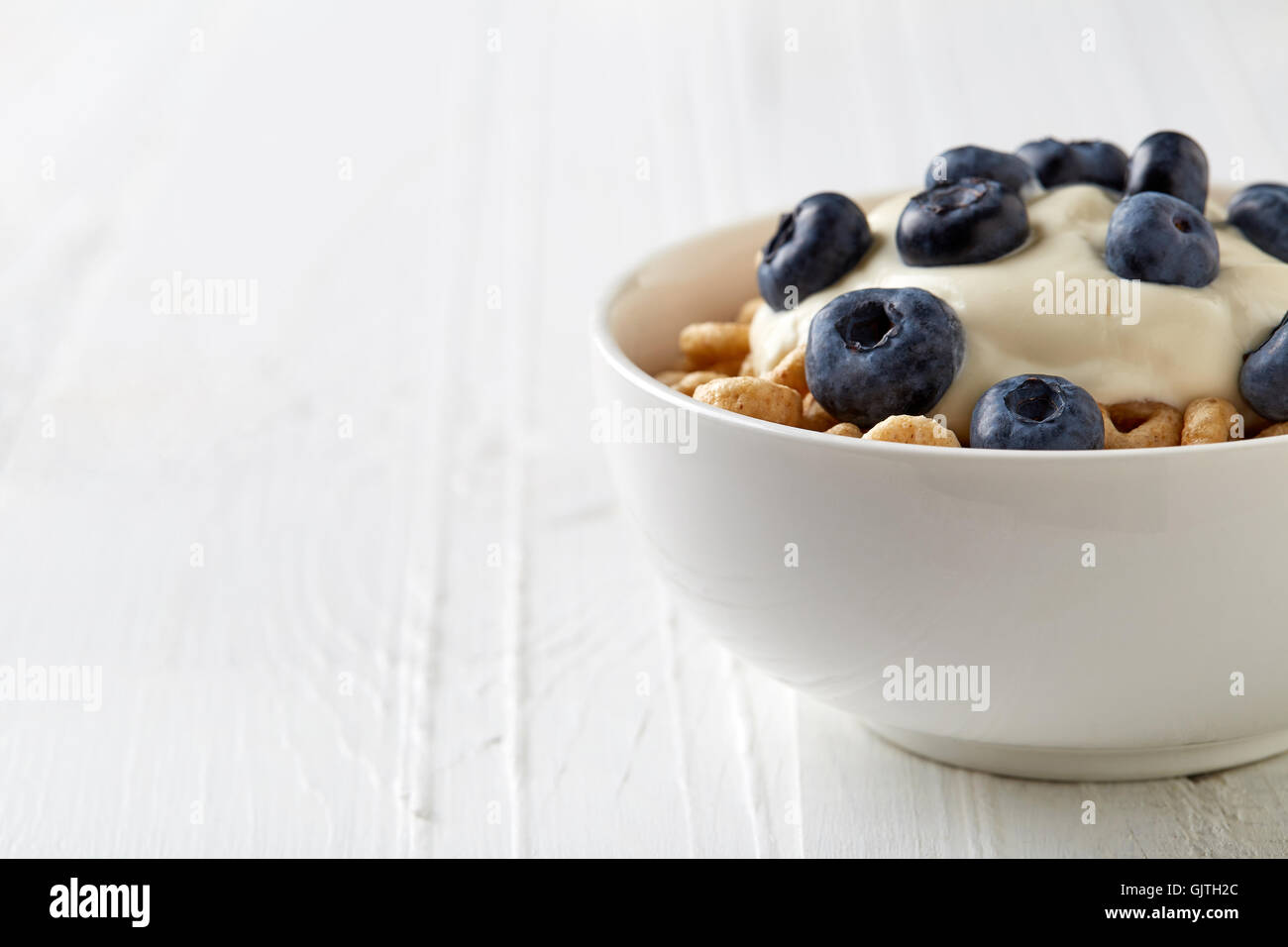 Ciotola di grano intero Cheerios a base di cereali con mirtilli e yogurt isolato su bianco tavolo in legno Foto Stock