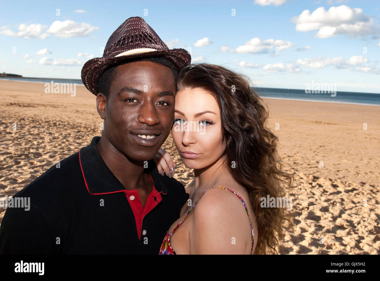 Coppia giovane multiculturale di razza mista di testa e spalle teste insieme guardando nella fotocamera sulla spiaggia emozioni romantiche Foto Stock