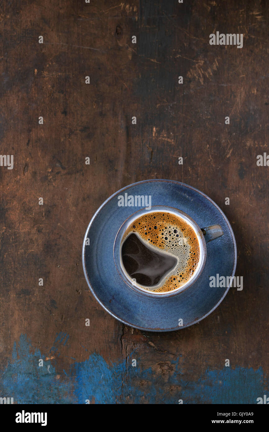 Blue coppa in ceramica di nero caffè caldo sul piattino, servita su un vecchio legno sfondo a trama. Semplice stile minimalista. Vista dall'alto. C Foto Stock