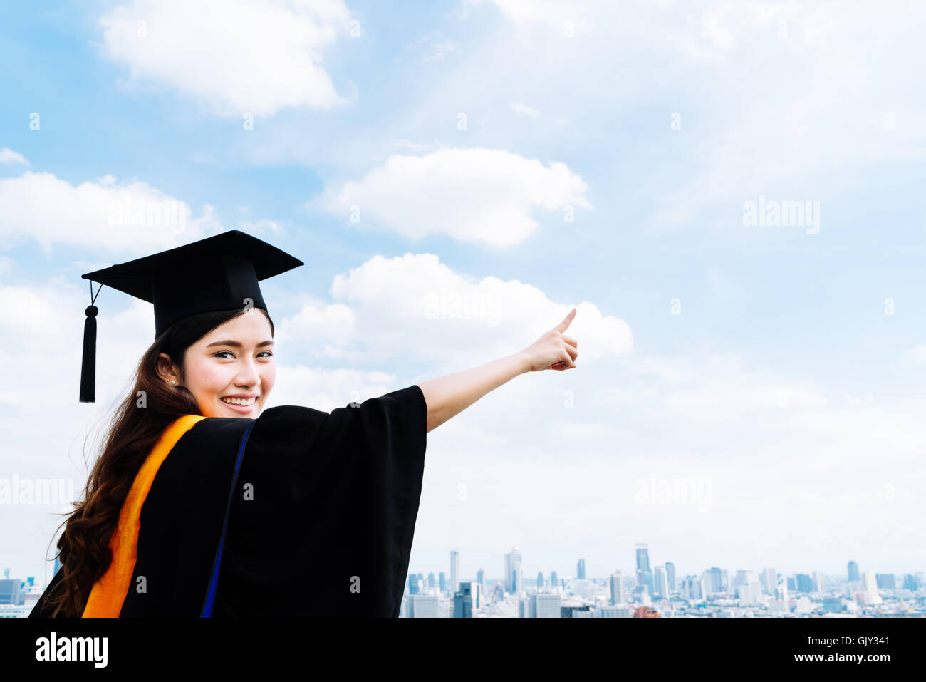 Bella asiatica università o college studente laureato donna nella graduazione abito accademico o camice, sorridente e puntando alla copia Foto Stock
