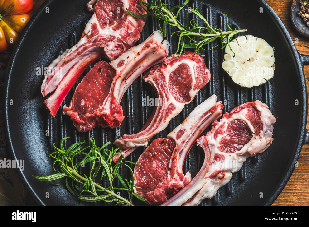Materie non cotti agnello costolette di carne di pollo con rosmarino e aglio in ferro nero padella per grigliare, vista dall'alto, composizione orizzontale Foto Stock