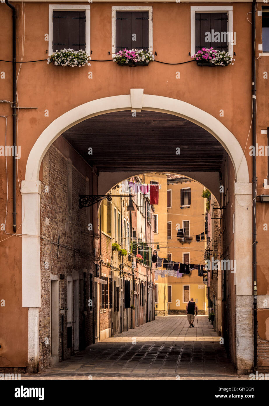 Uomo anziano a piedi con un bastone, al di sotto della linea di servizio lavanderia sospesa lungo il percorso. Venezia, Italia Foto Stock