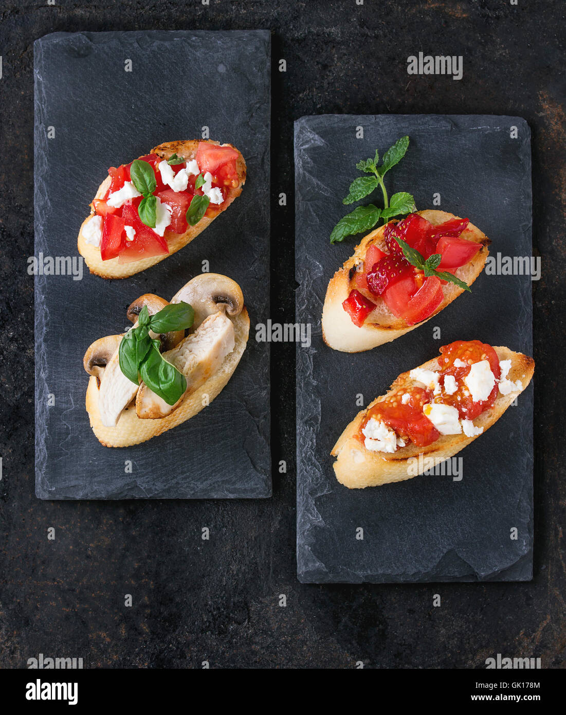 Varie di mini bruschette con pomodori, fragole, il formaggio feta, pollo, funghi e basilico sul baguette tostato, servita su Foto Stock