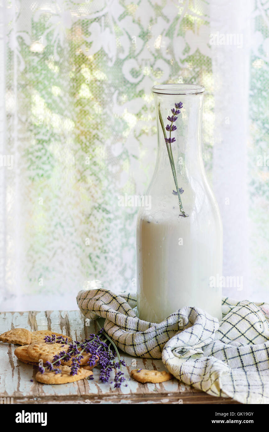 I cookie di lavanda e bottiglia di latte aromatico, servita con carta asciugatutto sul vecchio tavolo in legno con finestra in background. Prima colazione Foto Stock