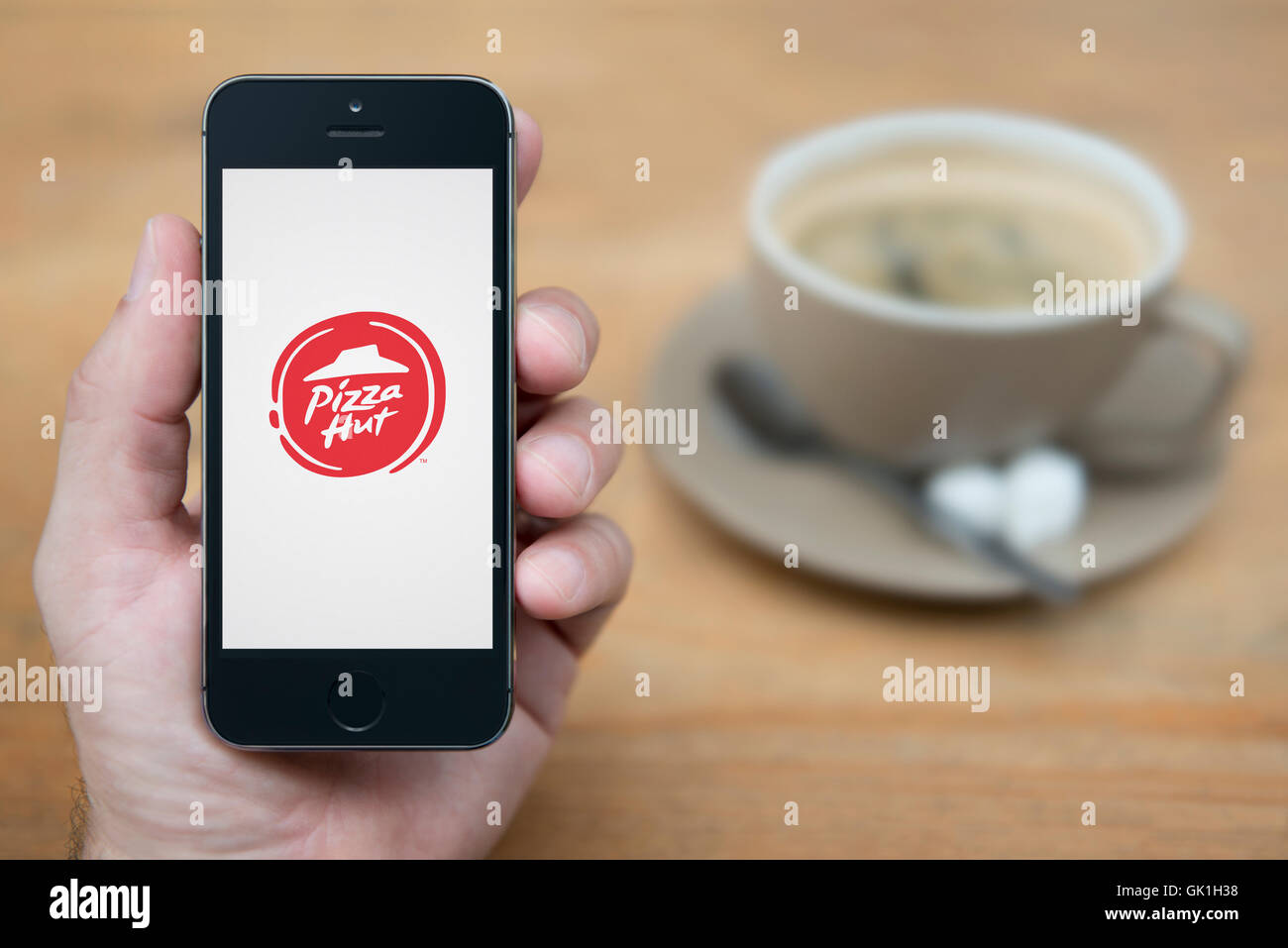 Un uomo guarda al suo iPhone che visualizza la Pizza Hut logo, mentre sat con una tazza di caffè (solo uso editoriale). Foto Stock