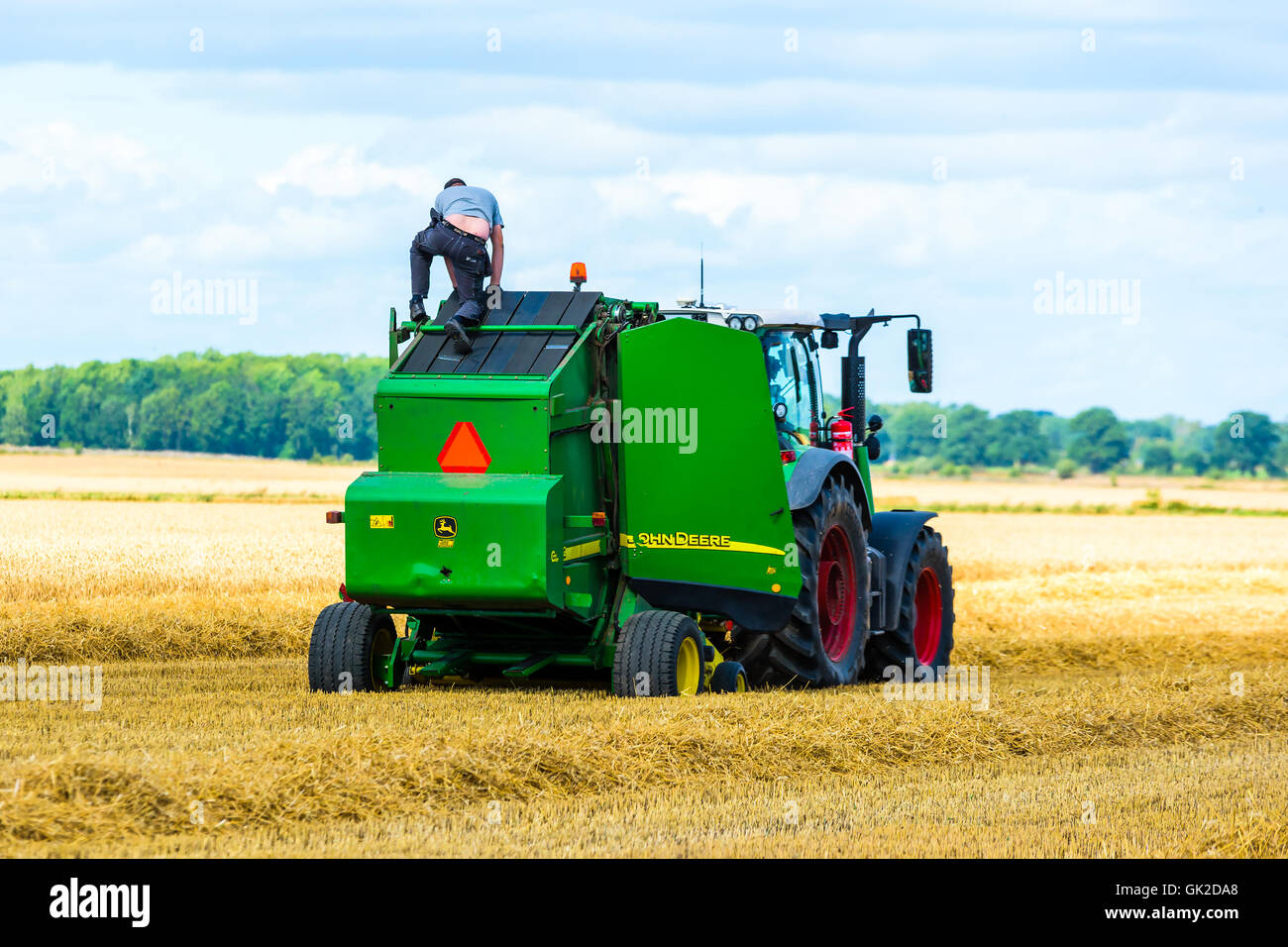 Kalmar, Svezia - 10 agosto 2016: nel campo della manutenzione di una imballatrice John Deere macchina che ha smesso di funzionare. Persona climbi Foto Stock