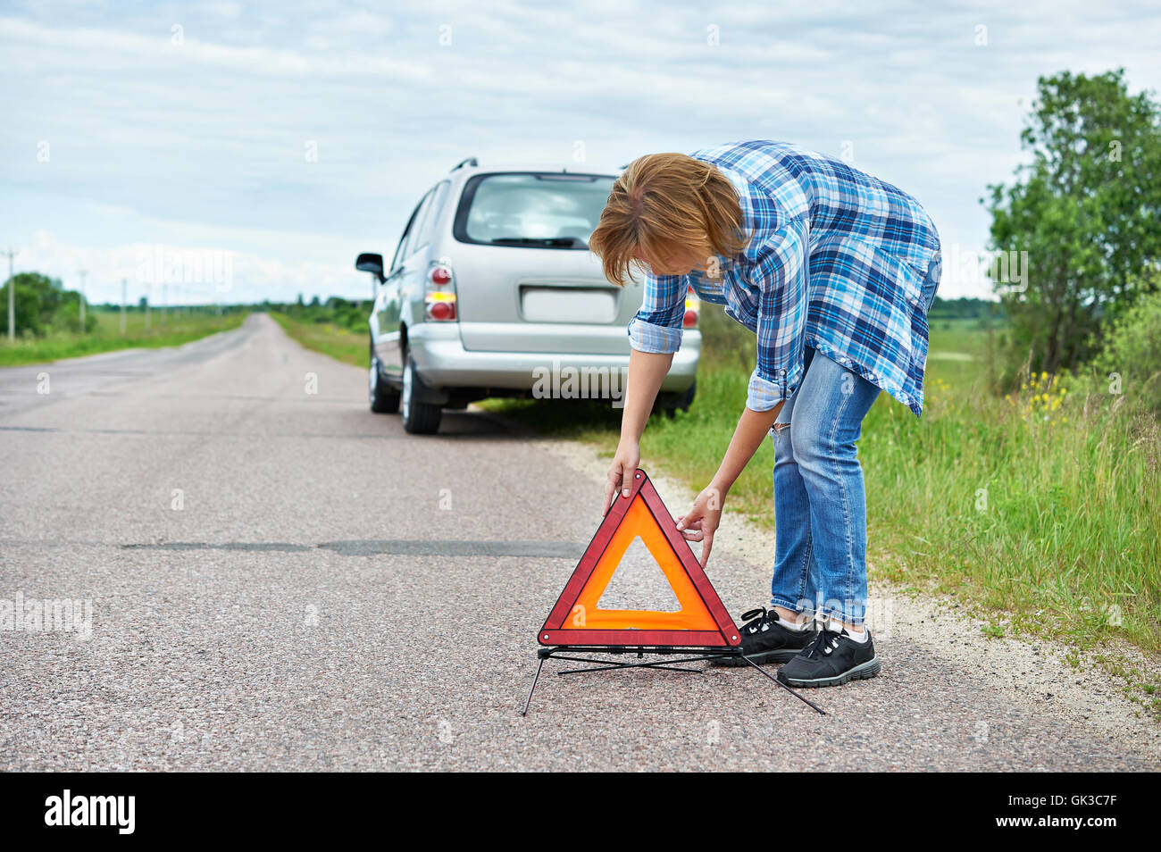 Donna installazione di segno di emergenza sulla strada vicino a Broken auto Foto Stock