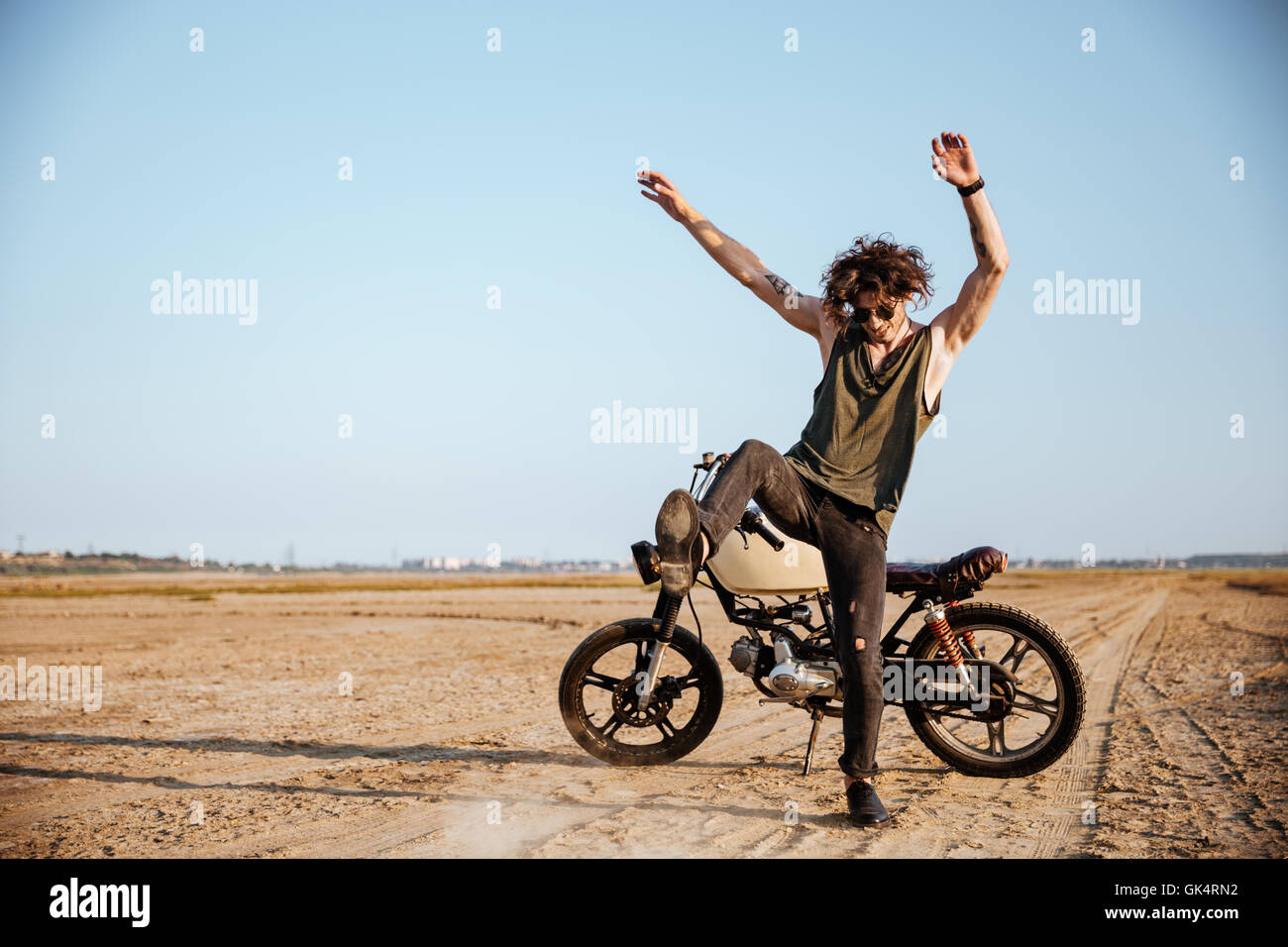 Uomo che fa la polvere in piedi vicino alla sua motocicletta in corrispondenza del deserto Foto Stock