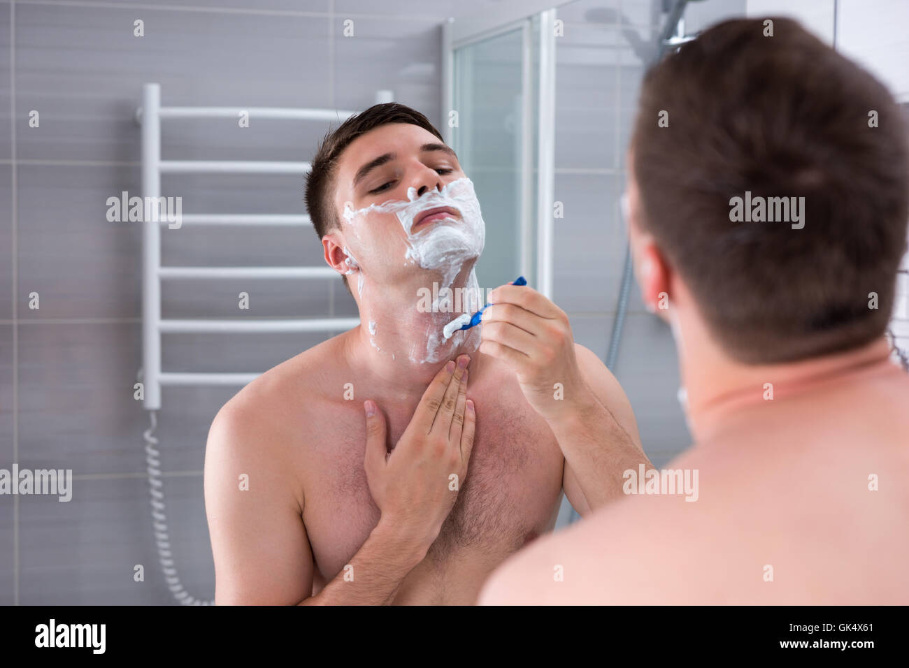 Uomo nudo la rasatura il petto e guardando lo specchio nel moderno bagno  rivestito di piastrelle a casa Foto stock - Alamy