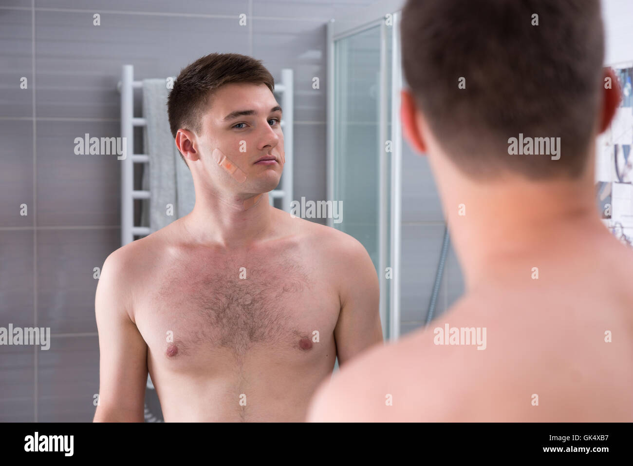 L'uomo dopo il brutto rasatura con band-aids sul suo volto in piedi di fronte allo specchio nel moderno bagno rivestito di piastrelle a casa Foto Stock