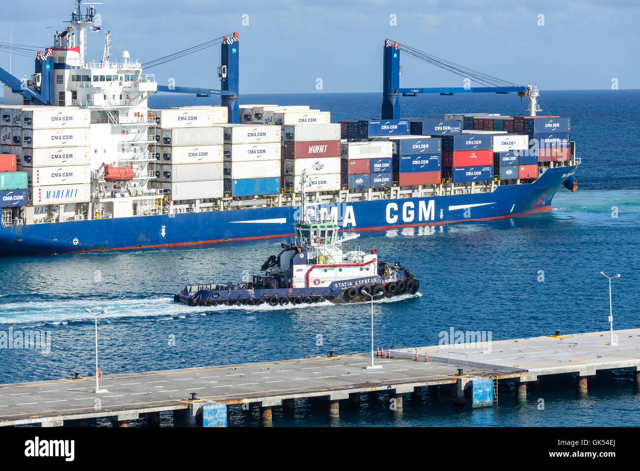 Un grande rimorchiatore lungo un enorme, caricato CMA CGM freighter in St Maarten Foto Stock