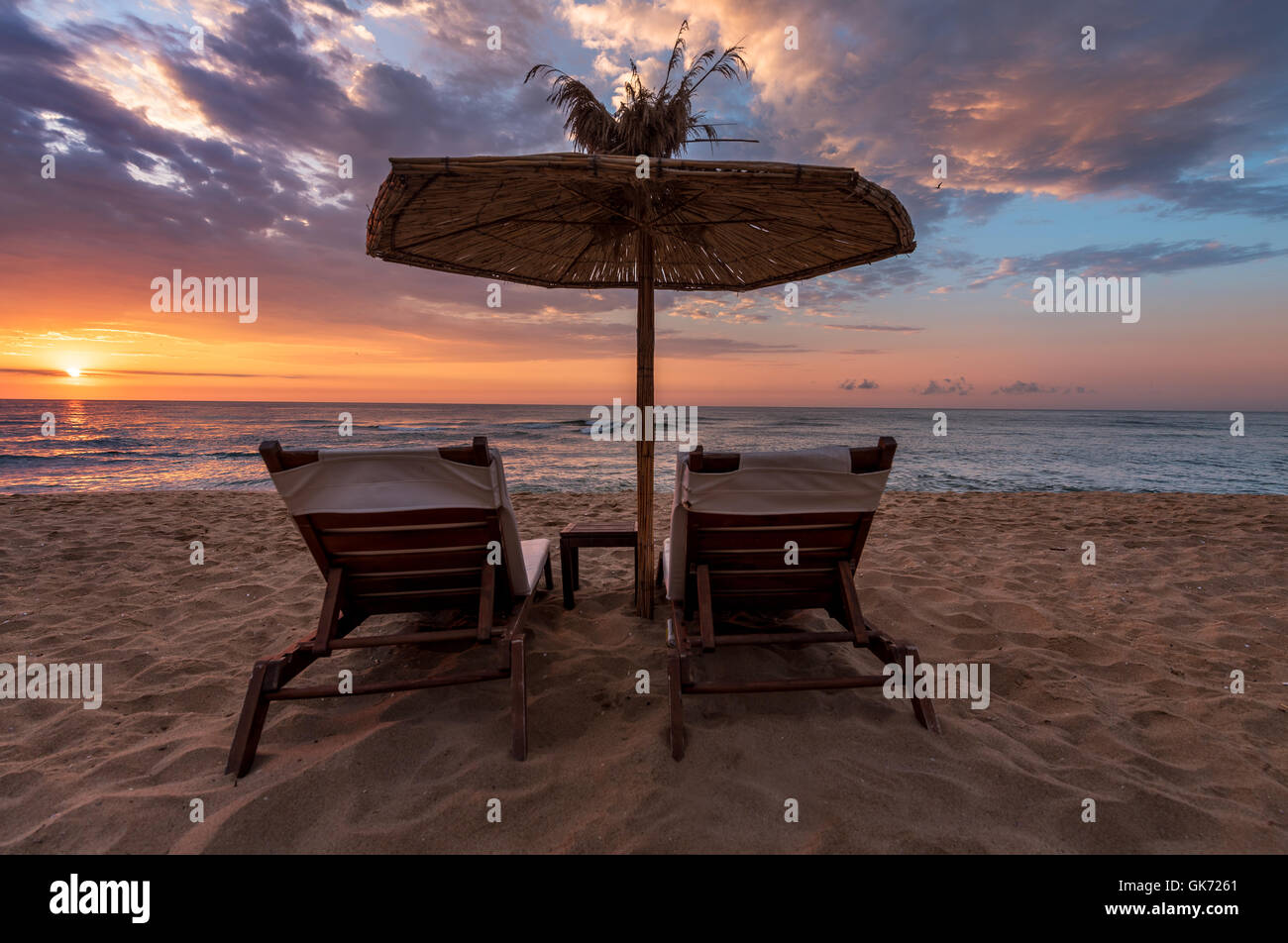 Vista posteriore di due sedie sdraio, lettini sotto ombrellone sulla spiaggia di sabbia. Foto Stock