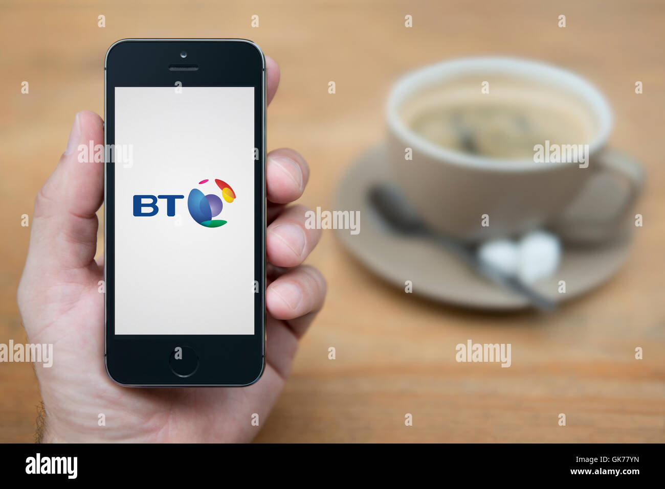 Un uomo guarda al suo iPhone che visualizza il logo di BT, mentre sat con una tazza di caffè (solo uso editoriale). Foto Stock
