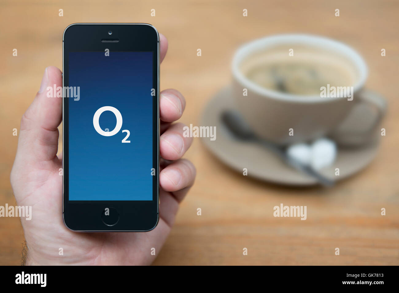 Un uomo guarda al suo iPhone che consente di visualizzare l'O2 logo, mentre sat con una tazza di caffè (solo uso editoriale). Foto Stock