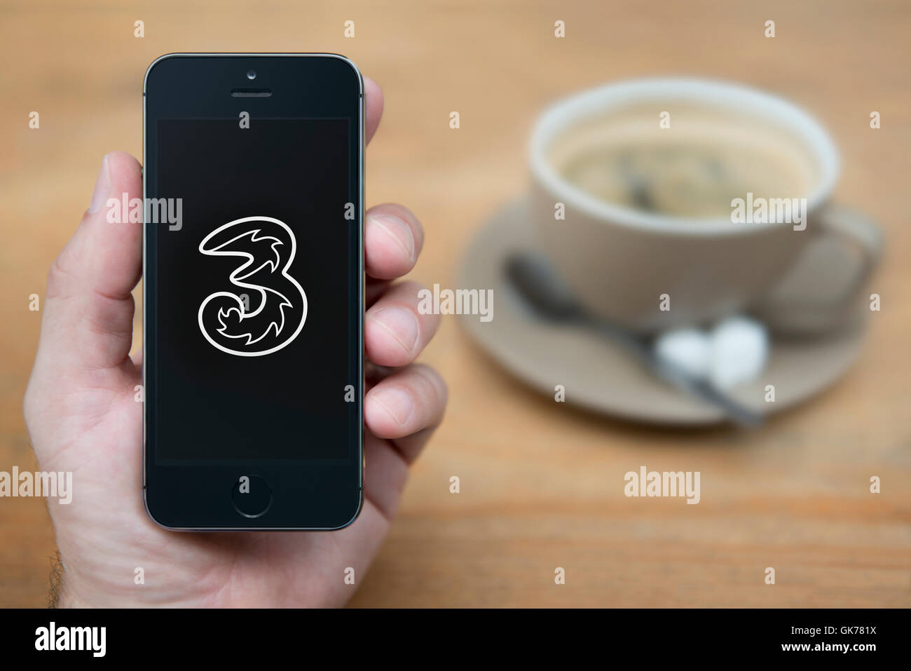 Un uomo guarda al suo iPhone che visualizza le tre logo mobile, mentre sat con una tazza di caffè (solo uso editoriale). Foto Stock