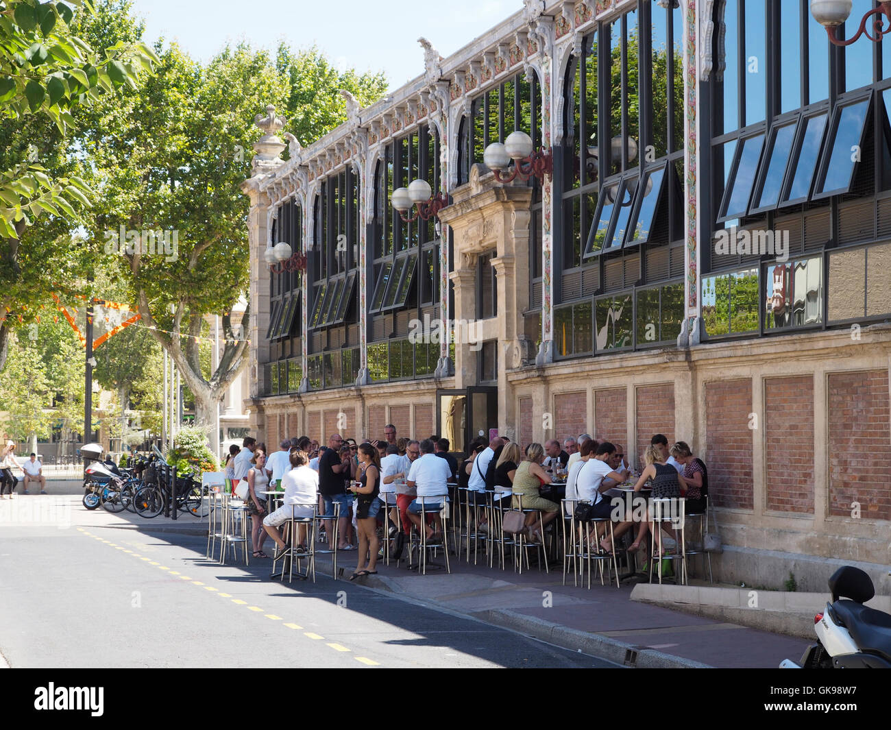 Le persone aventi il pranzo al di fuori di les halles il mercato alimentare di sale nel centro della città di Narbonne, Languedoc Roussillon, Francia Foto Stock