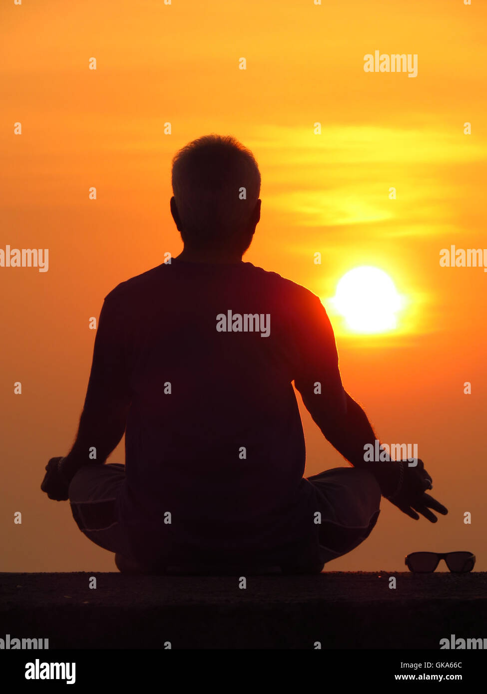 Un uomo meditando contro il sole di setting di un ritiro spirituale durante le vacanze estive Foto Stock