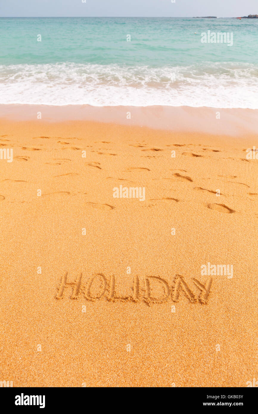 Bellissima spiaggia naturale dal blu del mare con iscrizione "vacanza" realizzato sulla sabbia Foto Stock