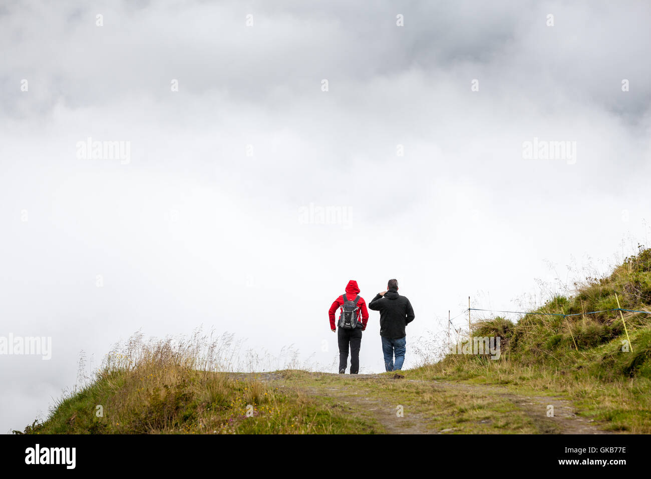 Persone da dietro a camminare su una pista di montagna di fronte a una fitta nebbia parete Foto Stock