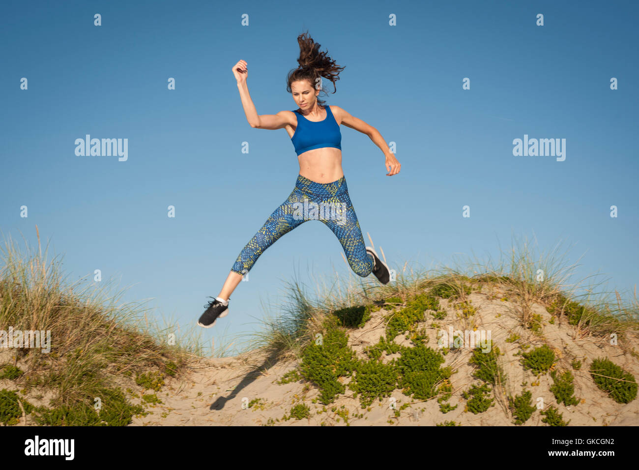 Donna che esercitano, correre e saltare in dune di sabbia Foto Stock