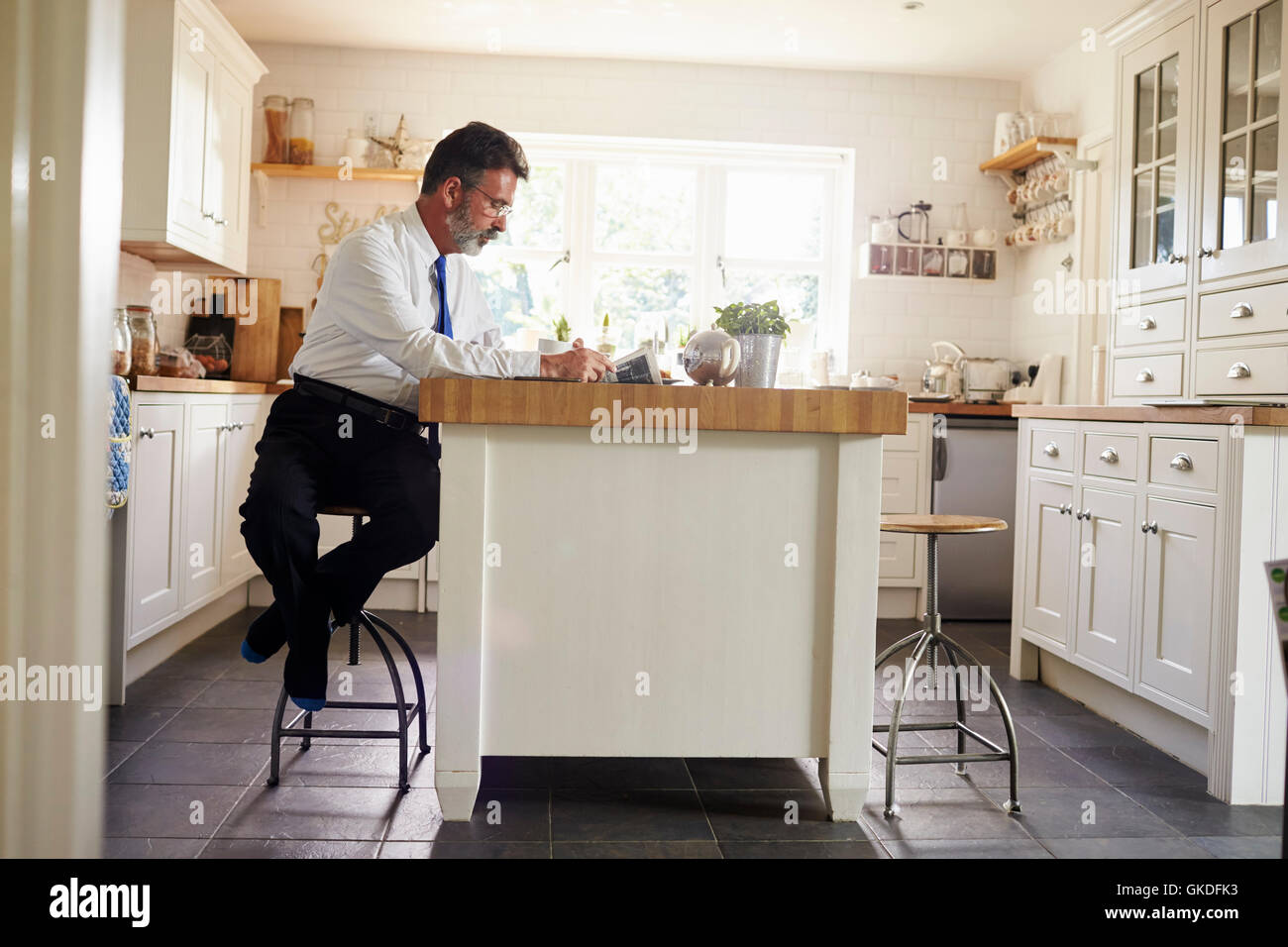 Uomo seduto in cucina isola la lettura prima del lavoro Foto Stock