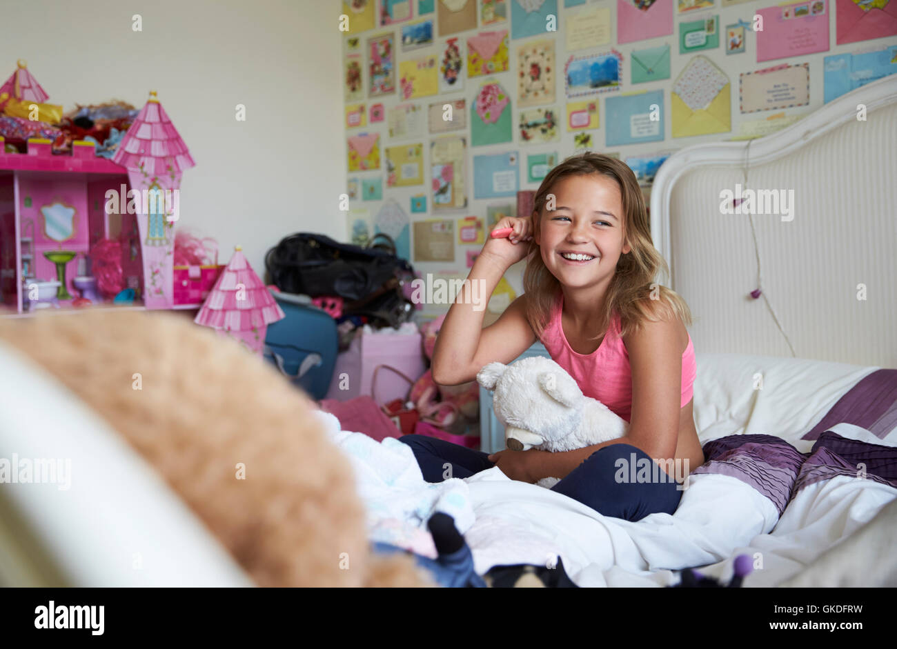 Sorridente ragazza seduta sul letto e spazzolare i capelli in camera da letto Foto Stock