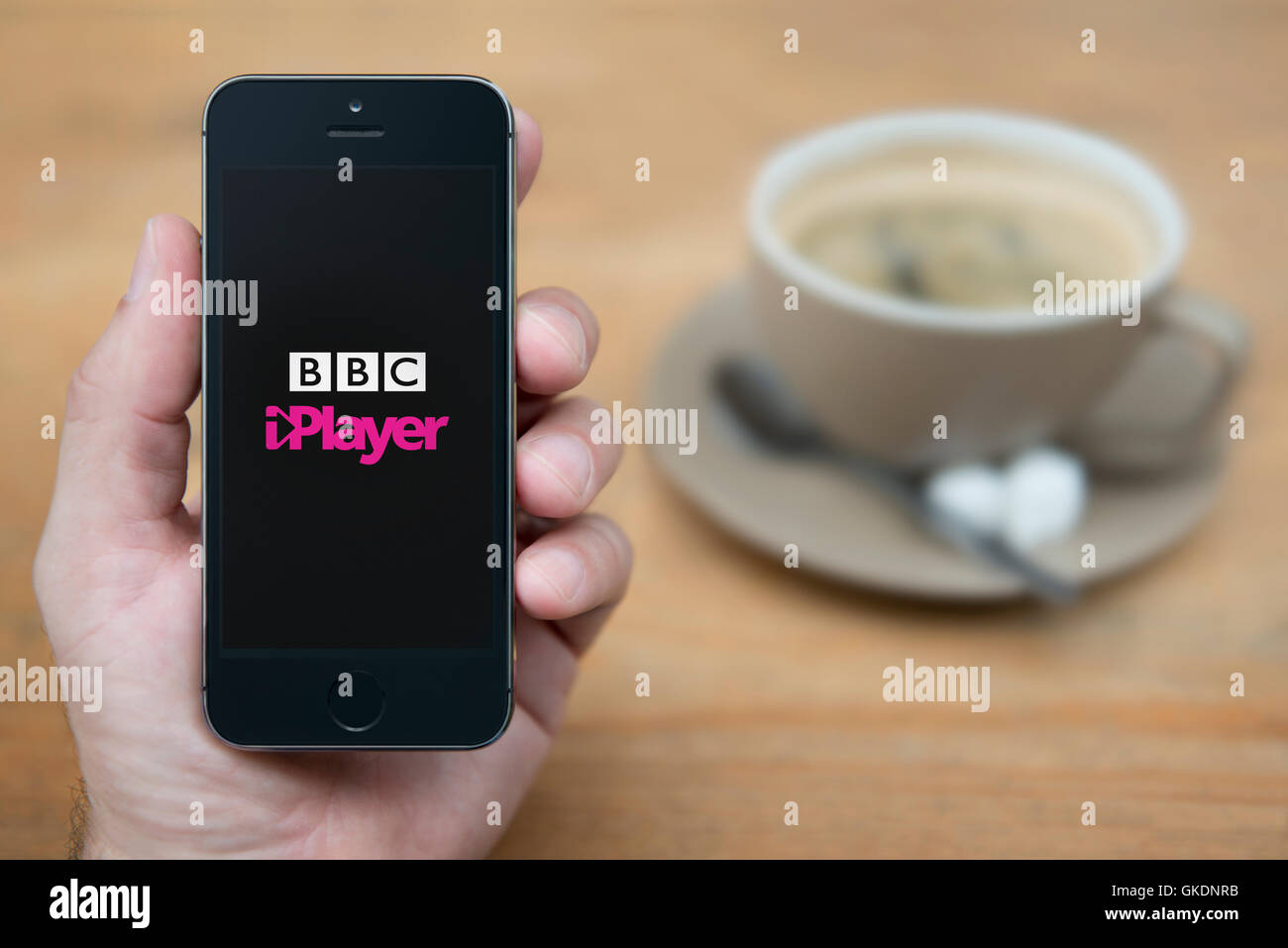 Un uomo guarda al suo iPhone che visualizza la BBC iPlayer logo, mentre sat con una tazza di caffè (solo uso editoriale). Foto Stock