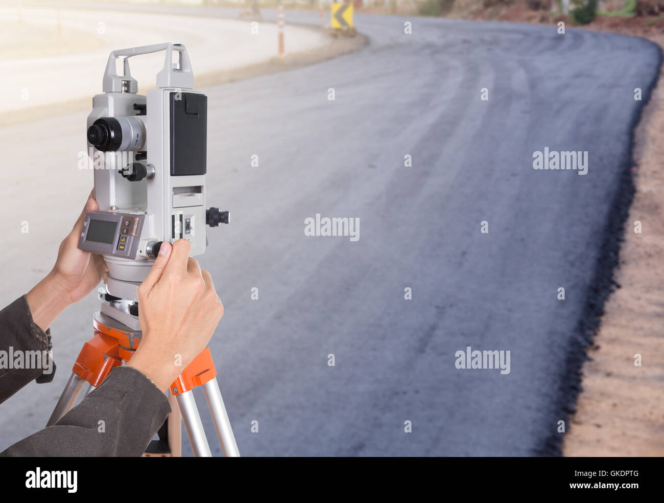 Lavorazione a mano con attrezzature di indagine teodolite su un treppiede. con la strada in costruzione sullo sfondo Foto Stock