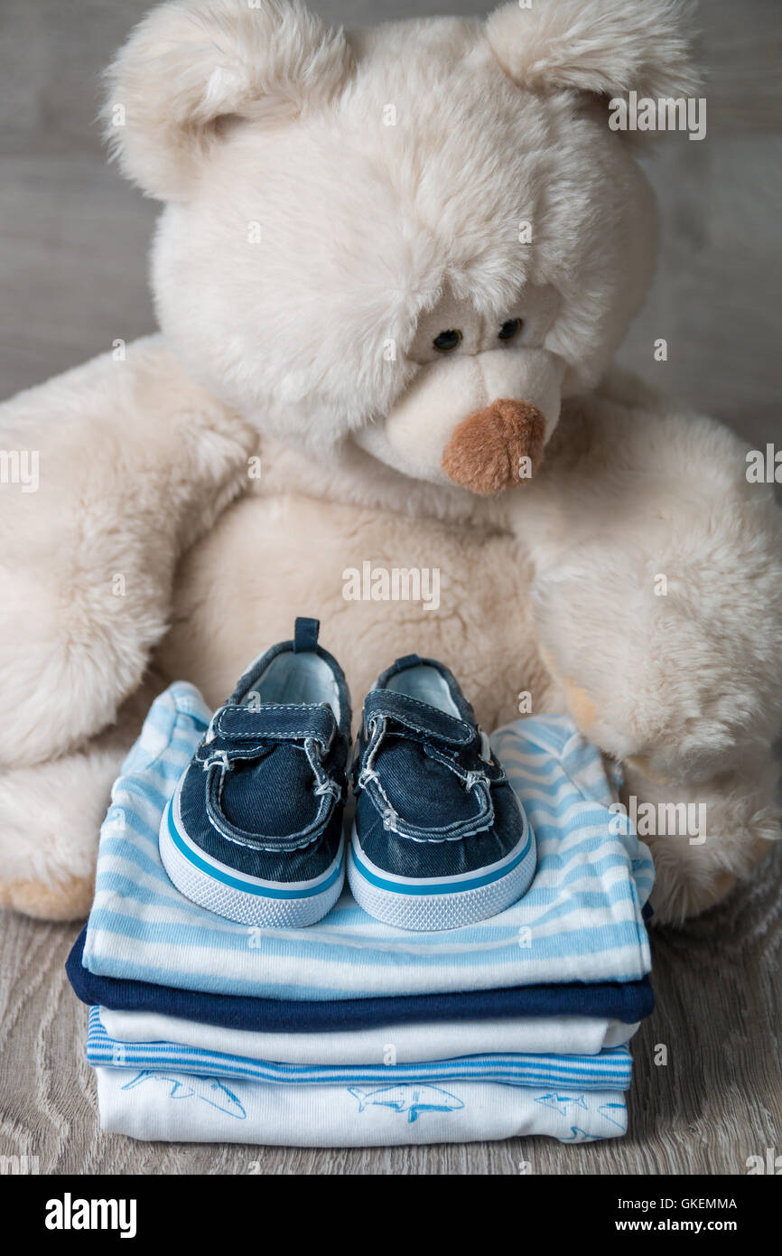Ripiegate blu e bianco body con le scarpe su di esso vicino al grande orso  di peluche sul grigio Sfondo di legno. pannolino per bambino neonato. stack  di Foto stock - Alamy