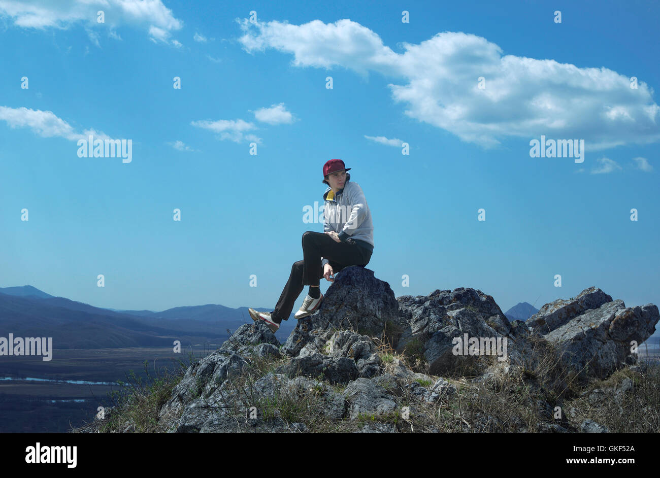 Giovane uomo sportive nel cappuccio rosso seduto sul picco di roccia arenaria e guardare i paesaggi della natura Foto Stock