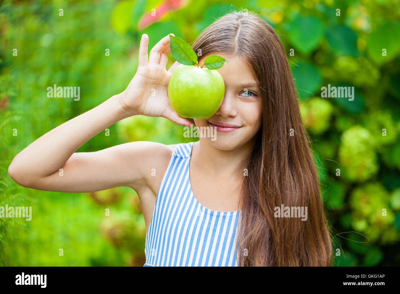 Happy brunette bambina con mela verde, estate all'aperto Foto Stock