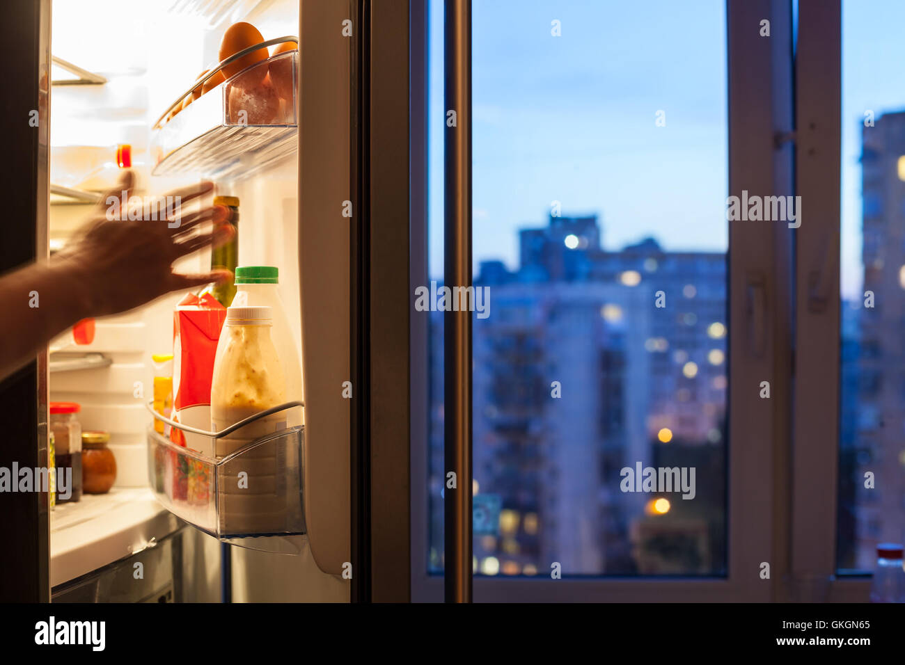 Invece arriva per alimenti in frigorifero e vista della città attraverso la finestra di casa in serata Foto Stock