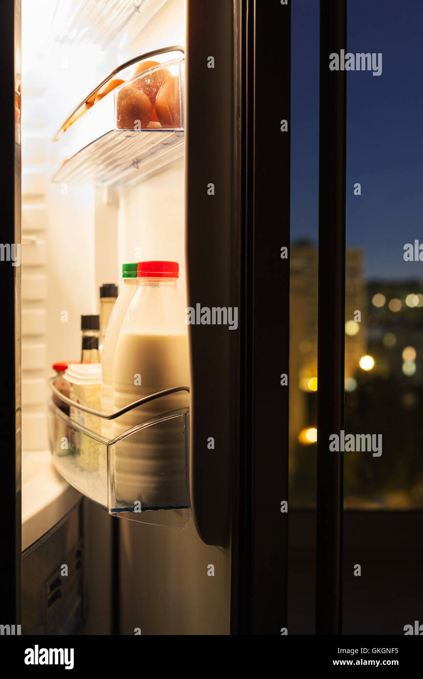 Aprire lo sportello del frigorifero con bottiglie di latte nella notte Foto Stock