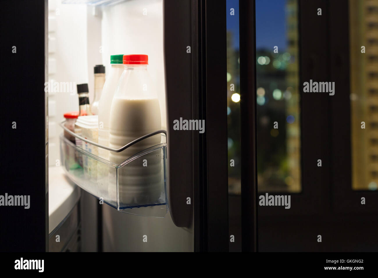 Aprire lo sportello del frigorifero domestico con bottiglie di latte nella notte Foto Stock