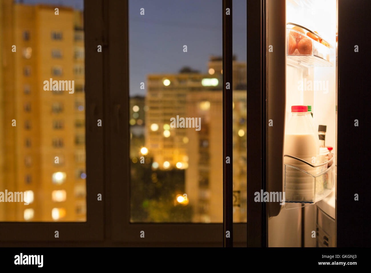 Aprire lo sportello del frigorifero domestico e urban vista attraverso il vetro di una finestra nella notte Foto Stock