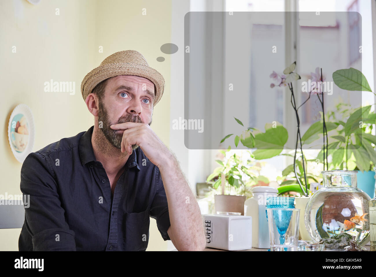L'uomo mcon con un fumetto pensiero sopra la sua testa seduto in una cucina in ambienti interni Foto Stock