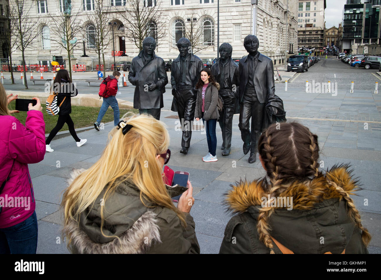 Turisti femmina per scattare delle foto al Beatles statua scultura al Pier Head sul lungomare Liverpools Foto Stock