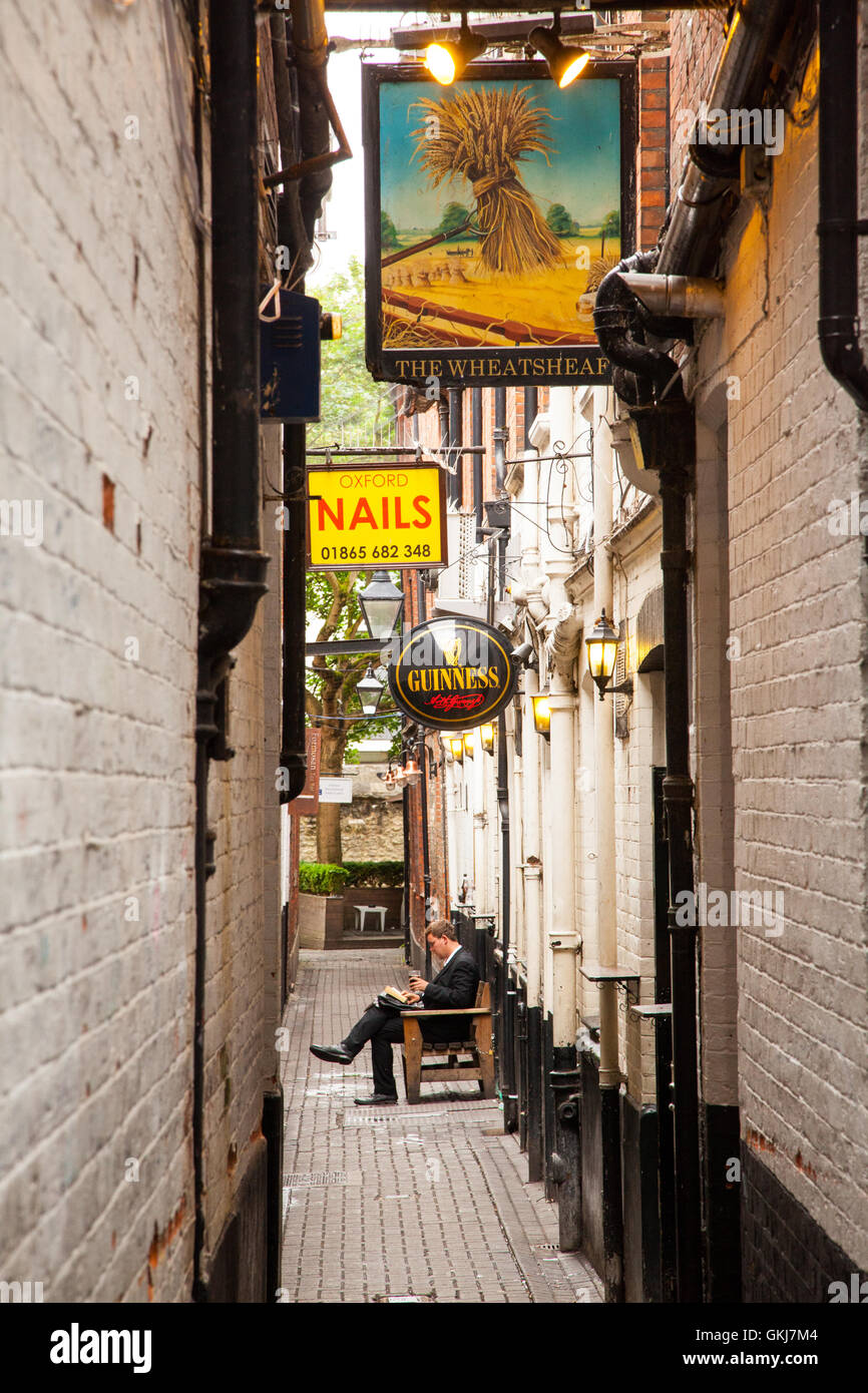 Uomo seduto a leggere un libro e bere un drink in un alleato fuori la Wheatsheaf pub nel centro di Oxford Foto Stock