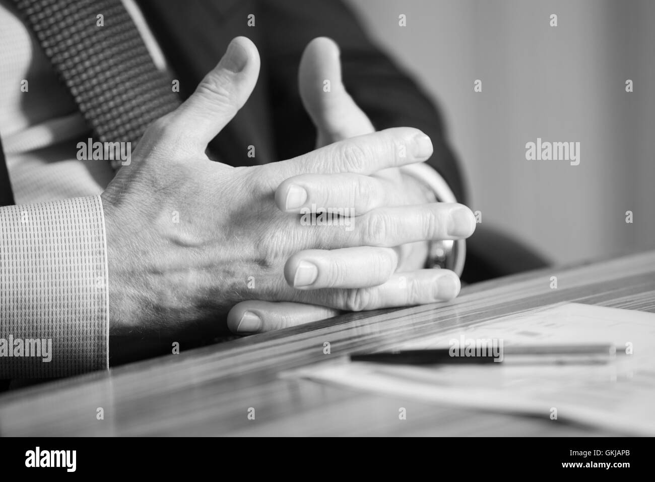 Uomo con le mani in mano in possesso di una penna nera in entrambe le braccia in un gesto di pensiero durante una riunione o negoziazione Foto Stock