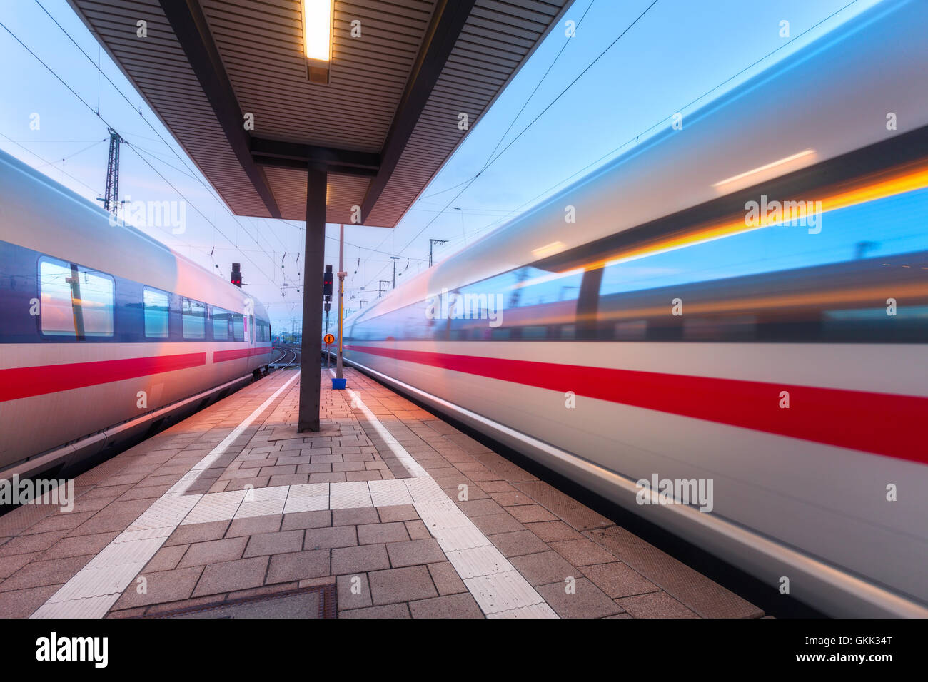 Alta velocità treni passeggeri sulla piattaforma ferroviario in movimento al crepuscolo. Treno sfocata. Stazione ferroviaria di notte Foto Stock