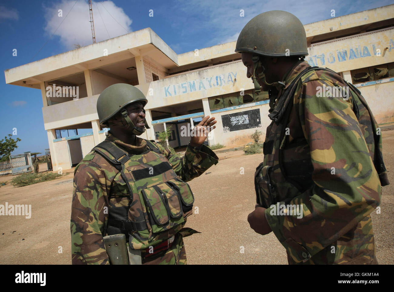 SOMALIA, Kismayo: in un handout fotografia rilasciato dall'African Union-United Nazioni Informazioni sul team di supporto 02 ottobre, i soldati del contingente keniota di servire con la missione dell Unione Africana in Somalia (AMISOM) stand davanti la bandiera nera di Al Qaeda affiliate del gruppo estremista al Shabaab dipinto sul muro di Kismayo Aeroporto. Keniote truppe AMISOM spostato dentro e attraverso Kismayo, finora ultimo urbano importante roccaforte di tAl Shabaab, sulla loro strada per l'aeroporto senza un colpo di essere licenziato a seguito di un'operazione di due mesi a liberare la città e villaggi di tutta la Somalia meridionale e Foto Stock