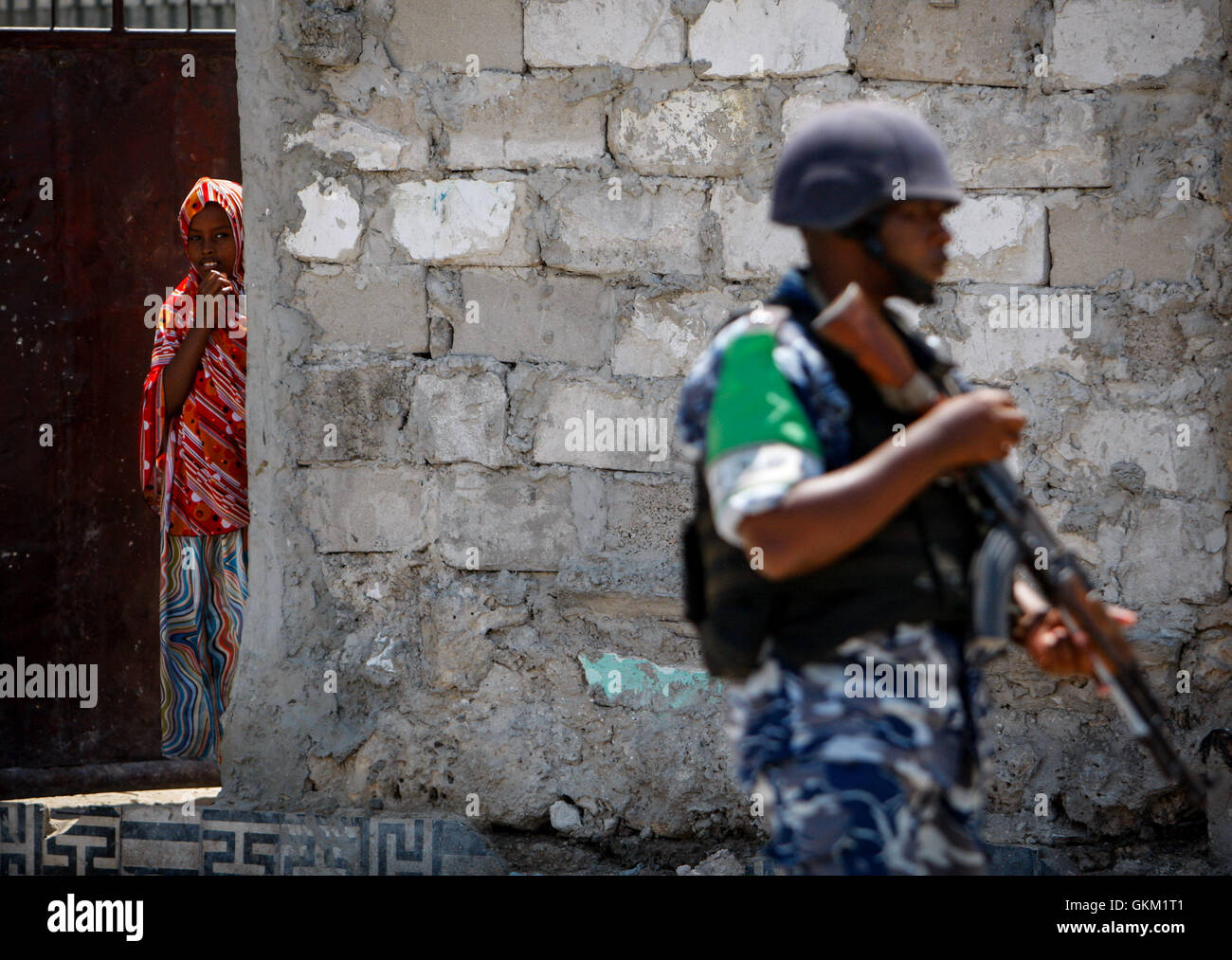 SOMALIA, Mogadiscio: in un handout foto scattata e rilasciato dall'African Union-United Nazioni Informazioni sul team di supporto 09 novembre, una giovane donna somala appare come un ugandese funzionario di polizia che serve come parte di un formato unità di polizia (FPU) con l'Unione africana Unione missione in Somalia (AMISOM) passeggiate passato durante una pattuglia di piede nel Kaa'correva nel quartiere della capitale somala Mogadiscio. Dell AMISOM FPUs stanno lavorando con i loro omologhi di forze di polizia somale (SPF) nel contribuire a fornire sicurezza a Mogadiscio in aggiunta a formazione e guida il SPF sulle attività di polizia tecniche e pratiche. AU-ONU MI Foto Stock