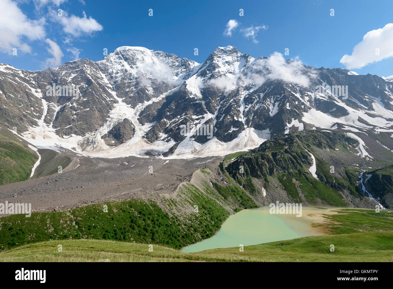 Il colore bluastro-verde lago di montagna contro un panorama di montagne coperte di neve e vette con i ghiacciai Foto Stock