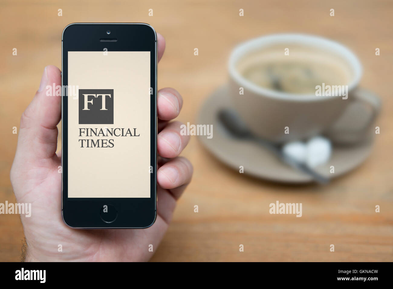Un uomo guarda al suo iPhone che visualizza il Financial Times logo, mentre sat con una tazza di caffè (solo uso editoriale). Foto Stock
