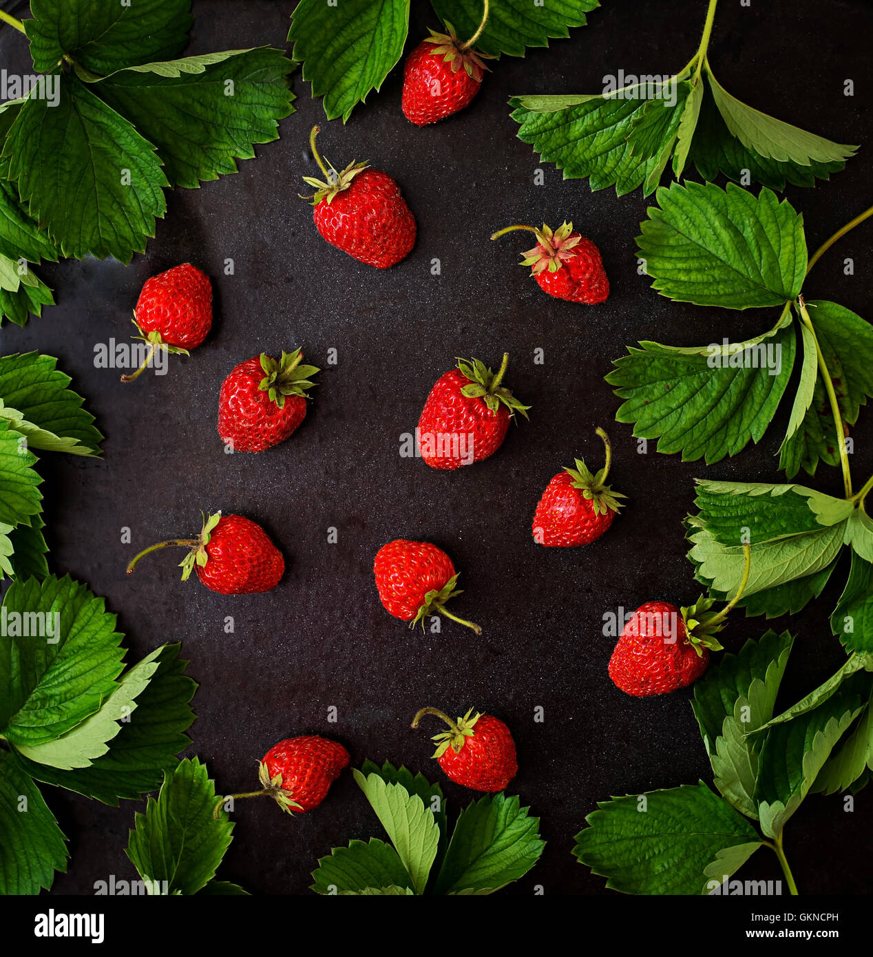 Fragole mature e foglie su uno sfondo nero. Vista superiore Foto Stock