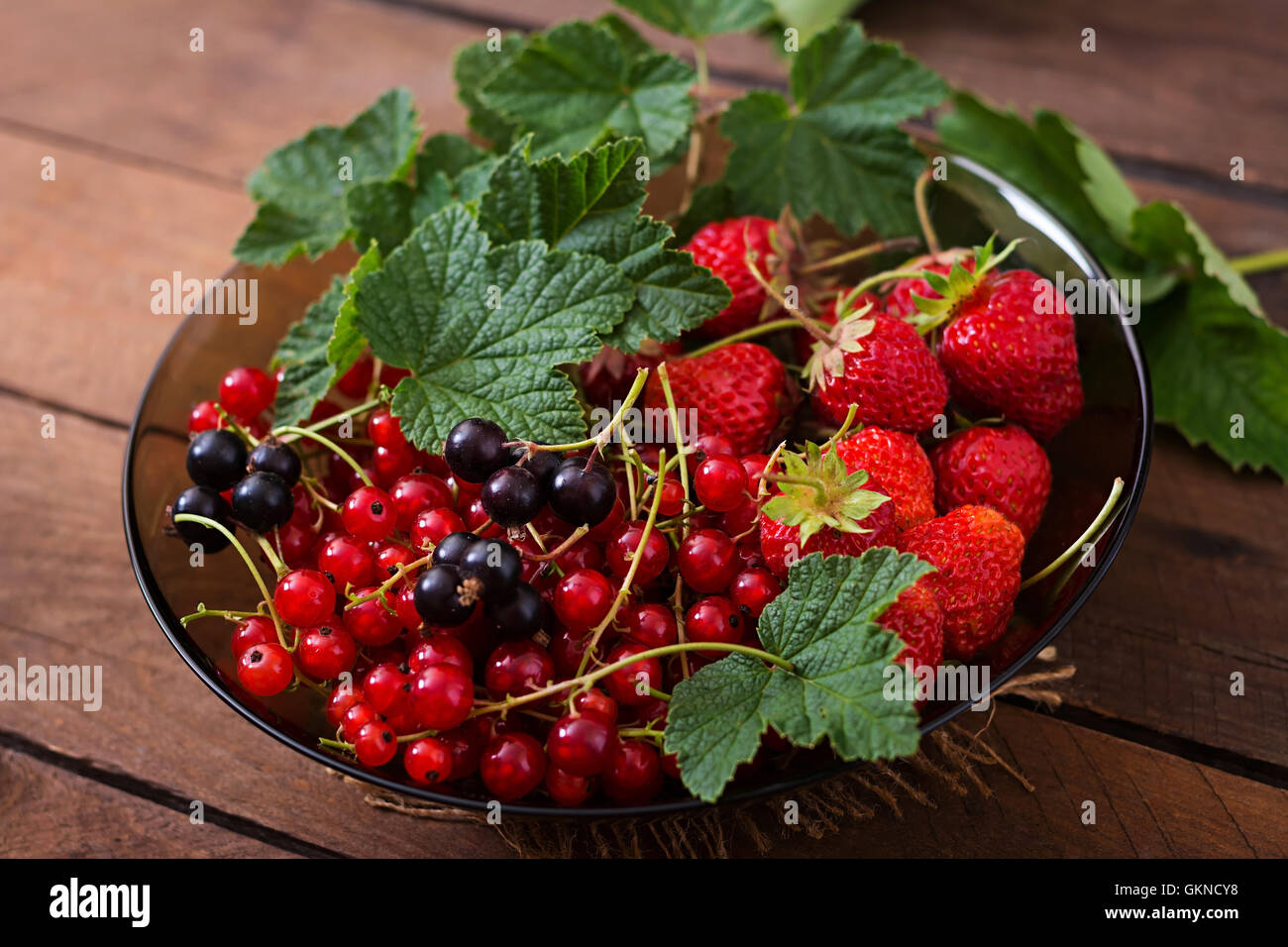 Piastra con frutti di bosco freschi (fragole e uve secche di Corinto) scuro su sfondo di legno Foto Stock
