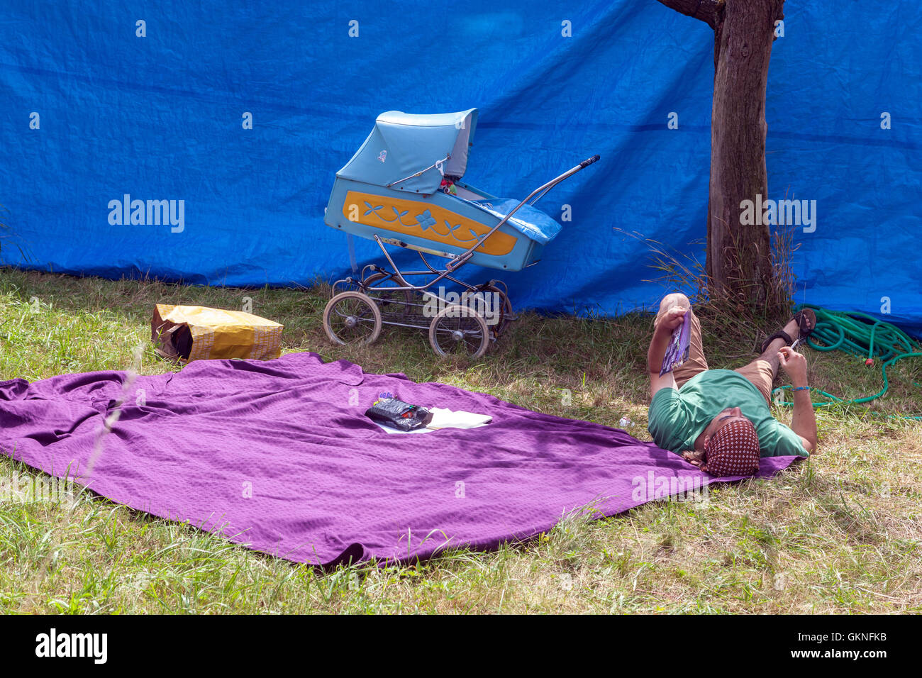 Babysitting, uomo sdraiato su una coperta e passeggino all'ombra di un muro blu, un idilliaco viaggio estivo in famiglia nella Repubblica Ceca Foto Stock
