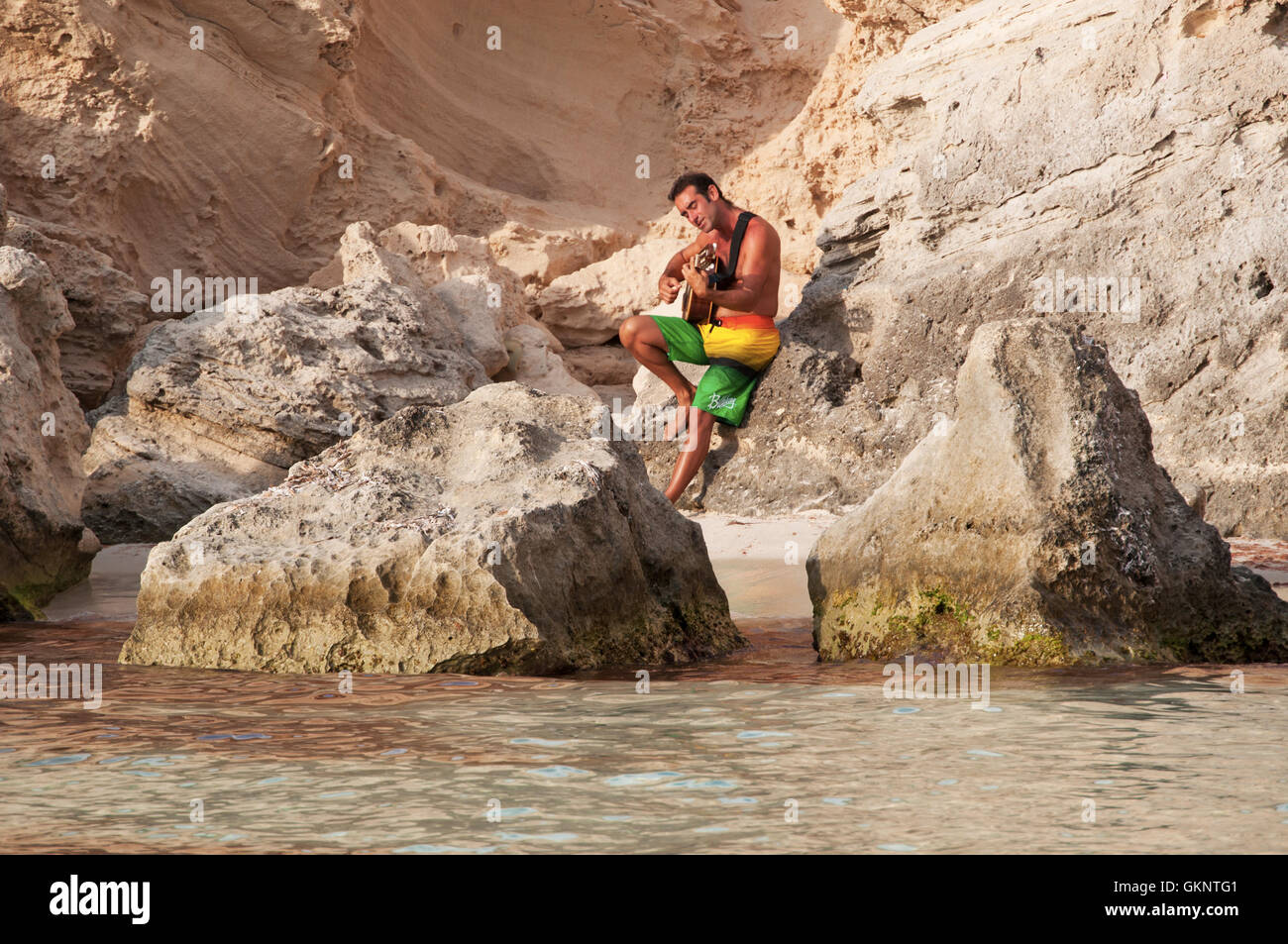 Formentera, isole Baleari: un uomo suonare la chitarra tra le rocce di Caló des Mort, una baia nascosta Foto Stock