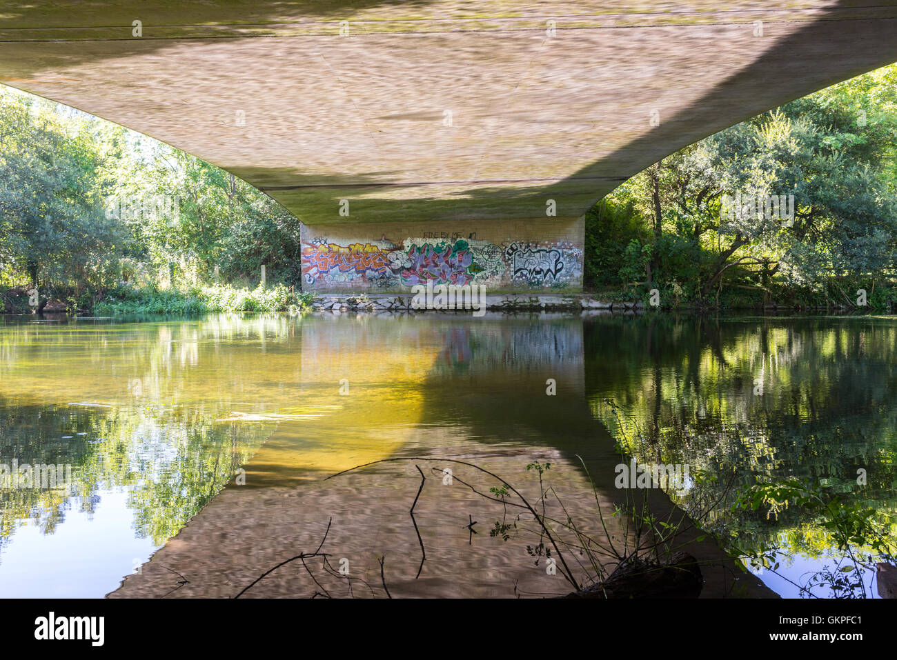 Graffiti su un muro sotto un cavalcavia ponte con luce solare e scintillante che si riflette sull'acqua di fiume per la struttura di calcestruzzo di cui sopra. Foto Stock