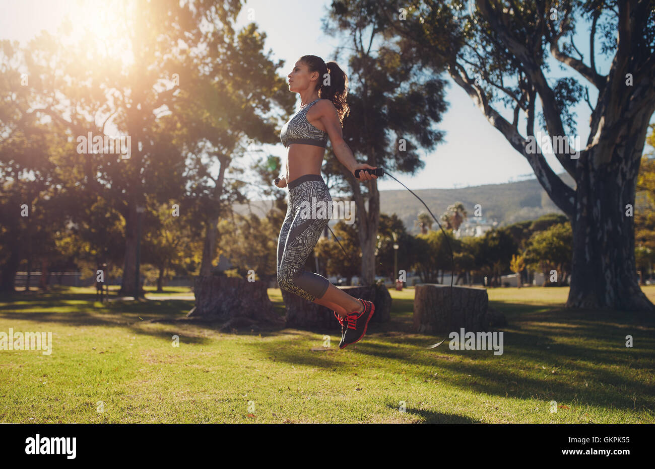 A piena lunghezza Ritratto di montare la giovane donna saltando con un salto con la corda nel parco in un giorno d'estate. Foto Stock